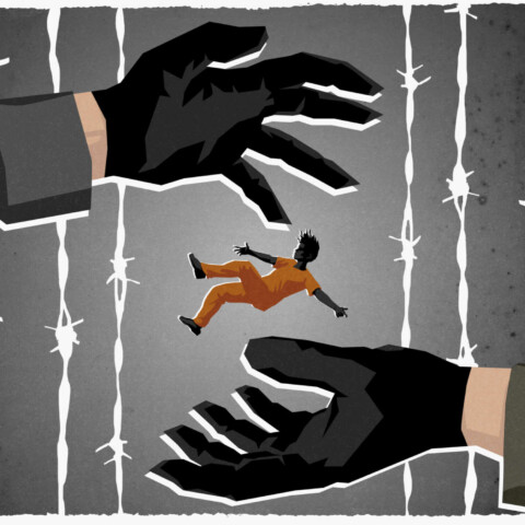 Gloved hands pass a prisoner between them with barbed wire in background