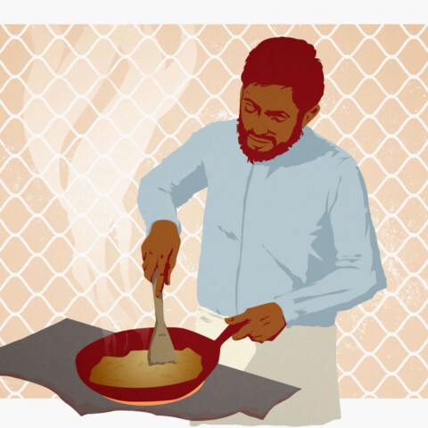 A man cooks a meal on a stove top with prison fencing backdrop